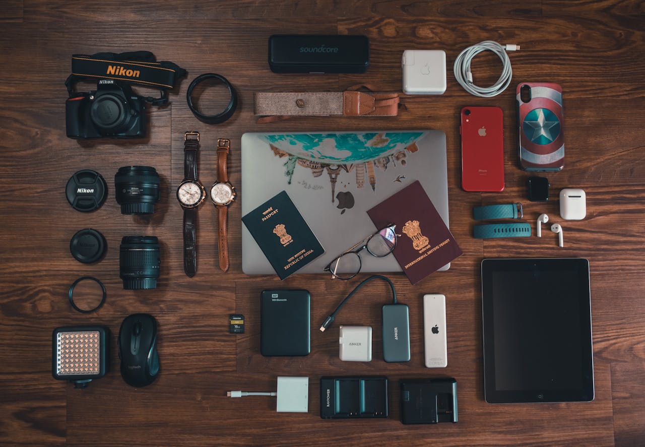 Passports, Camera, Battery Charger, Watches, and Cables on Brown Wooden Surface